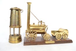 A vintage brass miners oil lamp together with a brass model of Stephensons Rocket on a plinth base