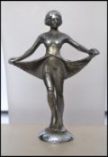 A silver white metal Art Deco car mascot in the form of a flapper girl raising her dress with