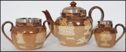 A Doulton Lambeth three piece stoneware harvest pattern tea service having silver rims being stamped
