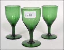 A trio of three 18th century Georgian Bristol green glass wine glasses each one raised on a plain