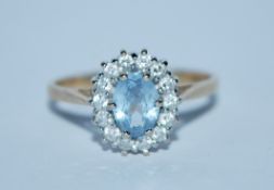 A hallmarked 9ct gold cluster ring set with a pale blue oval cut stone surrounded by a CZ halo.