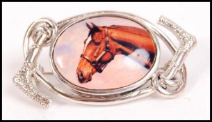 A ladies silver and enamel set dress brooch. The oval enamel pictorial of a horse ( hunting interest