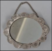 An Indian silver white metal small ladies vanity mirror on chain having a floral and leaf spray to