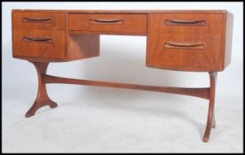 A 1970's G-Plan teak kneehole writing table desk raised on shaped supports with a series of drawers