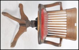 A 1930's Industrial oak office swivel chair being raised on a quadruped base with swivel column. The