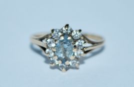 A hallmarked 9ct gold cluster ring set with a central pale blue oval cut stone surrounded by a white