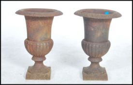 A pair of early 20th century campara cast iron urns raised on square bases with bulbous bodies and