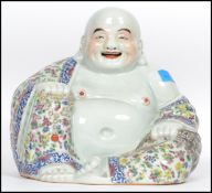 An Oriental ceramic large seated laughing Buddha decorated in famille rose patterned robes holding