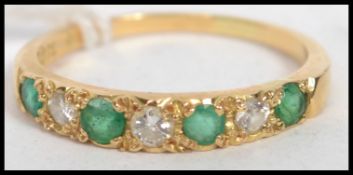 An emerald and diamond seven stone dress ring to an 18ct gold band, each cut diamond flanked by