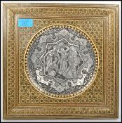 A 20th century silver white metal tondo panel depicting musicians and dancers set in a square gilt