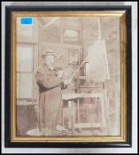 A framed and glazed photographic study of Sir Winston Churchill painting in his studio, stood next