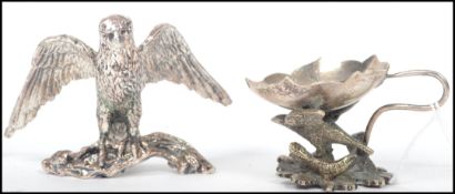 A silver white metal sculpture of an eagle perched on a branch along with a small leaf bowl raised