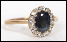 A 9ct gold, diamond and sapphire ring. The central sapphire of oval cut with a halo of diamonds