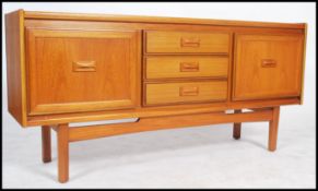 A retro G-plan style teak sideboard having drawers flanked by cupboards either side raised on shaped