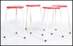 A set of four dot stool style stools, white coated tubular frames with a curricular red plastic