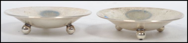 A pair of sterling silver pin dishes of concave circular form raised on three bun feet, makers