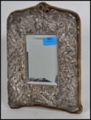 A silver easel mirror cast in relief with cherubs and putti with rococo scrollwork elsewhere. The
