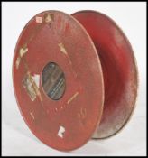 A vintage fire hose reel in red, having wall mount attached to one side.