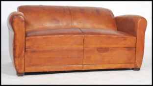 An early 20th century tan leather club sofa / settee having shaped sides and raised on square stub
