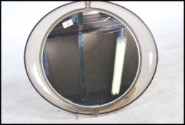 A vintage 20th century retro wall mirror of circular form being held in an oval smokey acrylic