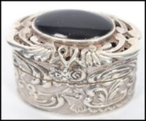 A silver hallmarked rococo influence pill box with pierced scrolled lid with large onyx cabochon