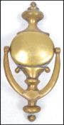 An early 20th century large brass door knocker of oval form with shaped finial top and swag drop,
