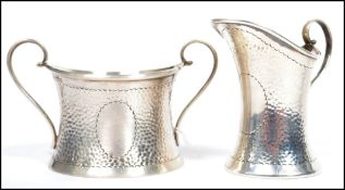 A silver hallmarked arts and crafts influence sugar bowl and creamer jug having scrolled handles