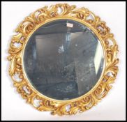 A 20th century circular bevelled glass mirror held within a highly ornate carved gilt frame
