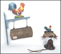 Two vintage 20th century cast iron welcome signs with cockerels atop, one having a bell and the