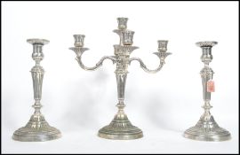 A set of three silver plated candle sticks and candelabras raised on circular bases with knopped