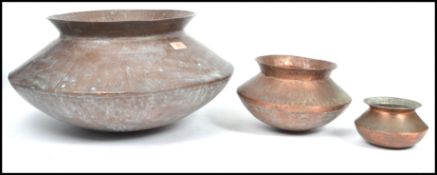 A collection of three early 20th century graduating hand beaten copper bowl / planters, bulbous body