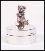 A sterling silver pill box of circular form having articulated teddy bear to lid. Weighs 19 grams.