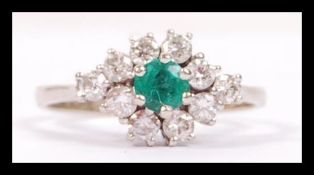 A white gold emerald and diamond cluster ring havi