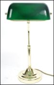A vintage 20th century bankers desk lamp having an adjustable green glass shade raised on a brass