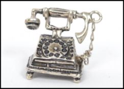 A silver miniature model of a ring dial telephone with phone to top.Weighs 7.7 grams. Measures 2