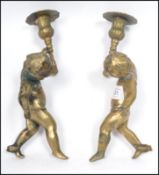 A pair of heavy brass candle sticks in the form of cherub putti's holding sconces with flared