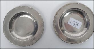 A pair of arts and crafts silver white metal hammered pin dishes of circular form with makers