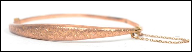 A hallmarked 9ct bracelet bangle having a half engraved decoration with safety chain. Weighs 4