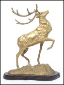 A vintage 20th century brass figurine of a stag with raised front leg and head set on a naturalistic