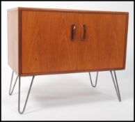 A 1970's retro teak wood 2 door cabinet being raised on tapered hairpin legs, each cabinet door with