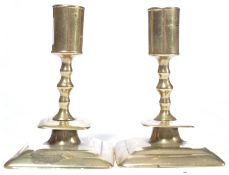 A pair of interesting 17th century brass candlesticks being raised on square bases, drop catchers