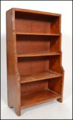 An early 20th century walnut Arts and Crafts inspired waterfall open dwarf bookcase, having four
