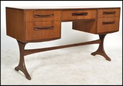 A 1970's G-Plan teak kneehole writing table desk raised on shaped supports with a series of