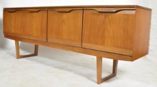 A 1970's retro teak wood sideboard of low and wide form being raised on tapering legs. Above, the