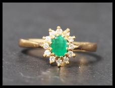 A hallmarked 18ct gold emerald and diamond cluster ring having a central oval cut emeralds