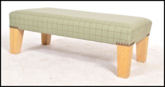 A contemporary upholstered beech wood footstool of rectangular form being upholstered in a green
