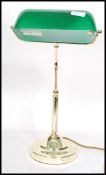 A vintage 20th century bankers desk lamp having an adjustable green glass shade raised on a brass