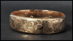 A 1/5th 9ct gold bangle bracelet having a full engraved design with safety chain and hidden clasp.