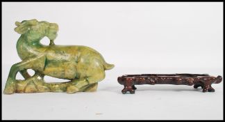 An early 20th century Chinese carved large green temple dog / oxon, raised on a carved hard wood