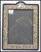 A silver hallmarked easel back picture frame having a bowed top with silver swirl and leaf
